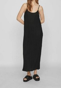 Zwarte geplooide maxi-jurk met dunne spaghetti-bandjes, een ontspannen pasvorm en een gladde textuur, gecombineerd met zwarte platform-sandalen.