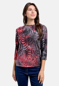 Mehrfarbiges Langarmoberteil mit einem wirbelnden Rosenmuster in Rot-, Grau- und Schwarztönen, aus einem weichen, strukturierten Stoff gefertigt.