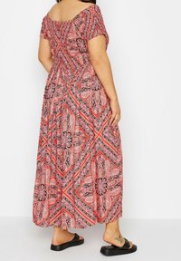 Maxiklänning med off-shoulder-design, prydd med ett blommönster i röd, svart och rosa, elastisk midja och korta ärmar. Bärs med svarta sandaler.