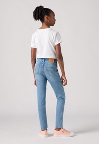 Jeans ajustados de color azul claro con pierna recta, camiseta blanca corta y zapatillas de deporte rosa claro. Etiqueta de cuero marrón notable en la parte de atrás.