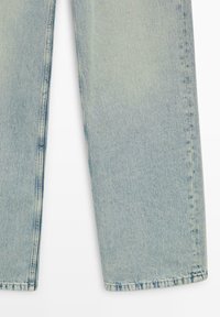 Jambes de jean en denim bleu clair avec coutures visibles, texture légèrement délavée, posées à plat sur un fond blanc.