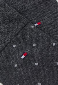 Calcetines gris oscuro fabricados en tejido suave, con patrones de puntos en blanco, gris claro y rojo, y un pequeño logo en rojo, blanco y azul.