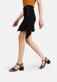 Sandali neri con tacco a blocco, dotati di una fascia di perline e una fibbia alla caviglia. Texture liscia, design open-toe e un tacco robusto per il supporto.