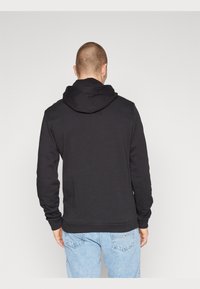 Sudadera negra con capucha ajustable, mangas largas, puños y dobladillo acanalados, llevada sobre unos jeans de mezclilla azul claro. Diseño minimalista, sin estampados.