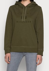 Sudadera con capucha de color verde oliva hecha de tela suave, con un logo frontal en letras oscuras, cordón ajustable y puños acanalados.