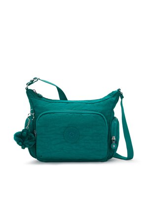 Blågrøn crossbody-taske med flere lynlåslommer, justerbar rem og en lille blød abe-vedhæng på hvid baggrund.
