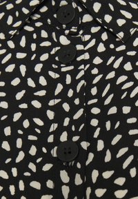 Camicia di tessuto nero con un motivo astratto bianco, dotata di colletto a punte e due bottoni neri lungo la parte anteriore.