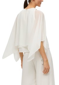 Biała bluzka z przezroczystymi, zwiewnymi rękawami i gładkim, dopasowanym przodzie. Zawiera małe zapięcie na guzik z tyłu przy szyi.