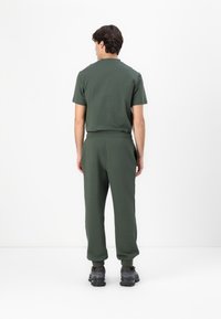 Camiseta de algodón verde oscuro y pantalones jogger a juego. La camiseta tiene cuello redondo; los pantalones jogger cuentan con una cinturilla elástica y puños ajustados. Zapatillas negras.