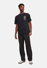 Sort bomulds t-shirt med et hvidt grafik på brystet, parret med løstsiddende mørke bukser og lyse sneakers.