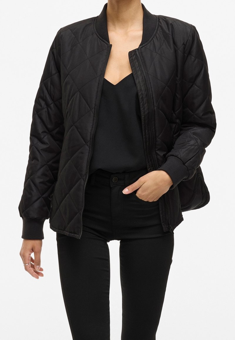 Černá prošívaná bomber bunda se zipem vpředu, žebrovanými manžetami a límcem. Disponuje hladkou texturou a detailem v podobě diamantového vzoru.