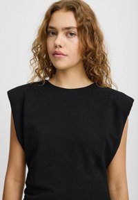 Černý bezrukávový top se strukturovaným designem ramenních částí, hladkou texturou a zaobleným výstřihem. Minimalistický styl a přiléhavý silueta.