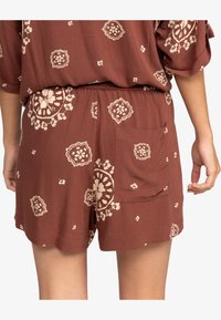 Shorts marron avec un motif floral crème, dotés d'une taille élastique et d'une seule poche arrière. Tissu léger, design ample.