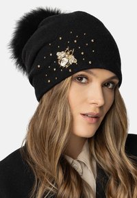 Căciulă din lână neagră cu un pompon pufoș, împodobită cu ținte aurii și un broșă decorativă în formă de albină, cu accente clare și aurii.