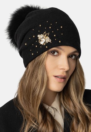 Beanie in lana nera con un pompon soffice, decorata con borchie dorate e una spilla a forma di ape con dettagli trasparenti e dorati.