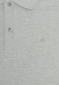 Polo gris clair texturé avec deux boutons gris et un petit logo brodé discret près de la poitrine.