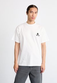 Camiseta de algodón blanca de mangas cortas, con un pequeño gráfico negro de una calavera y huesos cruzados en el lado izquierdo.