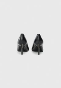 Zapatos de tacón alto de cuero negro con puntera afilada y tacón delgado. Presentan un diseño elegante y mínimos adornos. Textura suave. Vista trasera.