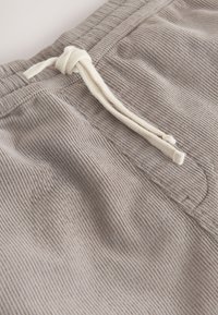 Gros plan d’un pantalon en velours côtelé beige avec une ceinture élastique et un cordon blanc noué.