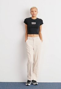 Svart avkortet t-skjorte med Nike-logo, beige høye bukser med livhøyde, og svarte sneakers med hvit såle. Glatt stoff, avslappet passform.