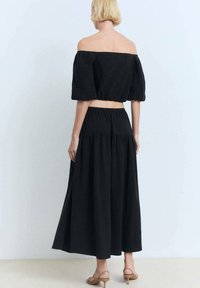 Ensemble noir en deux pièces comprenant un top court à épaules dénudées avec des manches bouffantes et une longue jupe avec une taille froncée.