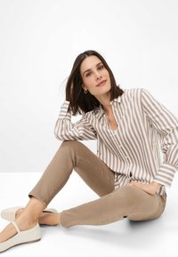 Camicia a righe beige e bianca, pantaloni fitted beige e scarpe basse di colore chiaro. Tessuto morbido e dettagli con bottoni sulla camicia.