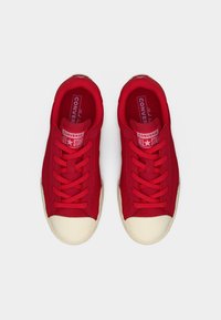 Ζευγάρι κόκκινα αθλητικά παπούτσια Converse All Star με λευκές λαστιχένιες μύτες και κόκκινα κορδόνια σε λευκό φόντο.