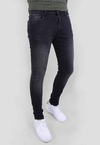 Vaqueros skinny de lavado oscuro, confeccionados en denim, con cierre frontal de cremallera, cinco bolsillos y detalles desgastados, combinados con zapatillas blancas.