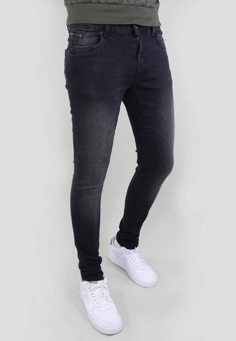 Vaqueros skinny de lavado oscuro, confeccionados en denim, con cierre frontal de cremallera, cinco bolsillos y detalles desgastados, combinados con zapatillas blancas.
