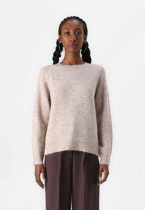 Pull en tricot texturé beige clair avec un col rond, des manches longues et une coupe décontractée. L'ourlet présente un motif côtelé.