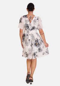 Vestido floral de tejido ligero con flores en negro y gris, espalda en V con cierre de lazo, mangas cortas y cintura smock.