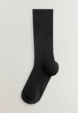 Černá ponožka z hladkého materiálu, s zesílenou patou a špičkou. Na vrcholu strukturovaný žebrovaný lem. Bez viditelných vzorů.