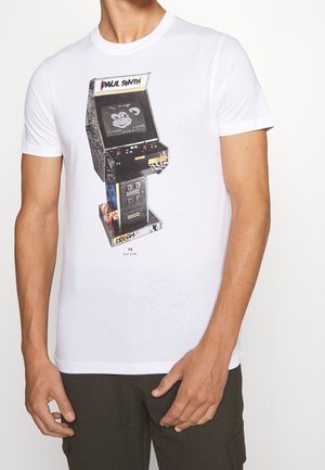 Mężczyzna noszący białą koszulkę z kolorową grafiką vintage automatu do gier i napisem „Paul Smith” z przodu.