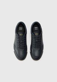Navy Leder Sneakers mit perforiertem Zehenbereich, goldenen Logo auf der Zunge, dunklen Schnürsenkeln und weißen Akzenten an der Sohle, die ein elegantes Design aufweisen.