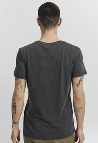 Mørkegrå bomulds t-shirt med korte ærmer, rund hals og en let tekstureret overflade; har synlige tatoveringer på begge arme.