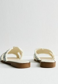 Vita sandaler med en mjuk pälsliknande textur och silverdekorationer. Platt träsoffa med ett lagerdesign, öppen bakdel och sidor.