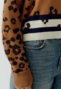 Bruine gebreide trui met een luipaardprint en een gestreepte onderrand in marineblauw, crème en bruin. Gecombineerd met blauwe denim jeans.