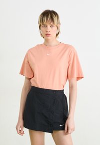 Light coral cotton t-shirt with short sleeves, featuring a small white Nike logo. Paired with a black wrap skirt, button details on the side.