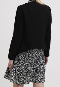 Černá přiléhavá bunda s hladkou texturou, v kombinaci s bílou a černou šaty s leopardím potiskem. Bunda má dlouhé rukávy a zkrácený střih.