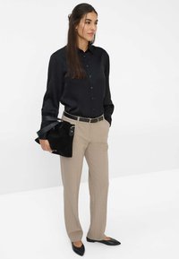 Schwarze satinierte Knopfbluse, beigefarbene maßgeschneiderte Hose, schwarze Wildledertasche mit Riemen, spitze schwarze Ballerinas. Klare Linien und weiche Texturen.