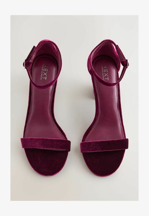 Fuksijos aksominiai aukštakulniai sandalai su atvira nosimi, kulkšnies dirželiu ir plačia priekių juosta. Lygus odos padas ir minkštas, tekstūruotas paviršius.