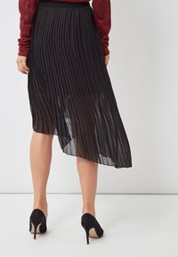 Falda midi negra con pliegues y dobladillo ligeramente asimétrico, hecha de material ligero, llevada con zapatos de tacón altos negros.