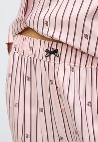 Cămașă și pantaloni de pijama cu dungi roz, realizați dintr-un material moale, având dungi bordo închis, accente cu brand și o fundă pe talie.