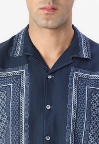 Navy short-sleeve shirt with decorative white patterns, featuring a pointed collar, button closure, and textured fabric.