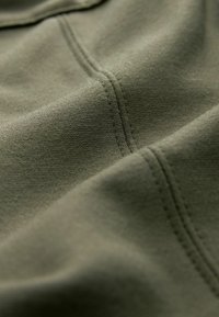 Tela verde oliva con una textura suave y costuras visibles. El material parece suave y ligeramente elástico, mostrando un brillo sutil.