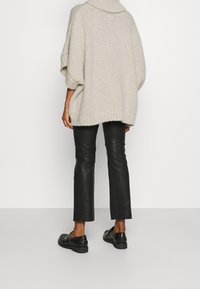 Übergroßer, cremiger Strickpullover mit hohem Kragen, kombiniert mit schwarzen Lederhosen und schwarzen Lackloafers. Weiche Textur, lockerer Schnitt.