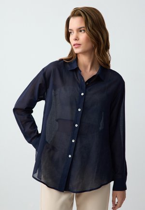 Navy blue, sheer button-up shirt with a collar, long sleeves, and rounded hem. Features white buttons and a light, textured fabric.