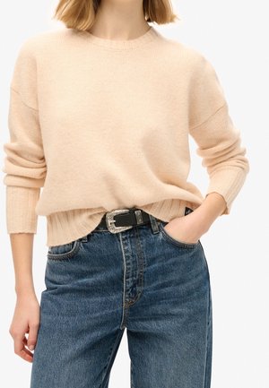 Pull en tricot pêche clair avec ourlet et poignets côtelés, associé à un jean taille haute bleu foncé et une ceinture noire avec une boucle en argent ornée.