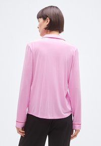 Cămașă cu mâneci lungi din țesătură roz deschis cu textură fină, având un guler și bordură contrastantă pe manșete.