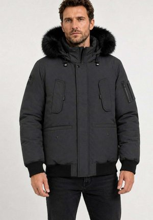 Homme portant une veste d'hiver noire avec une capuche doublée de fourrure, fermetures éclair et à boutons, et poches à l'avant et sur la manche.
